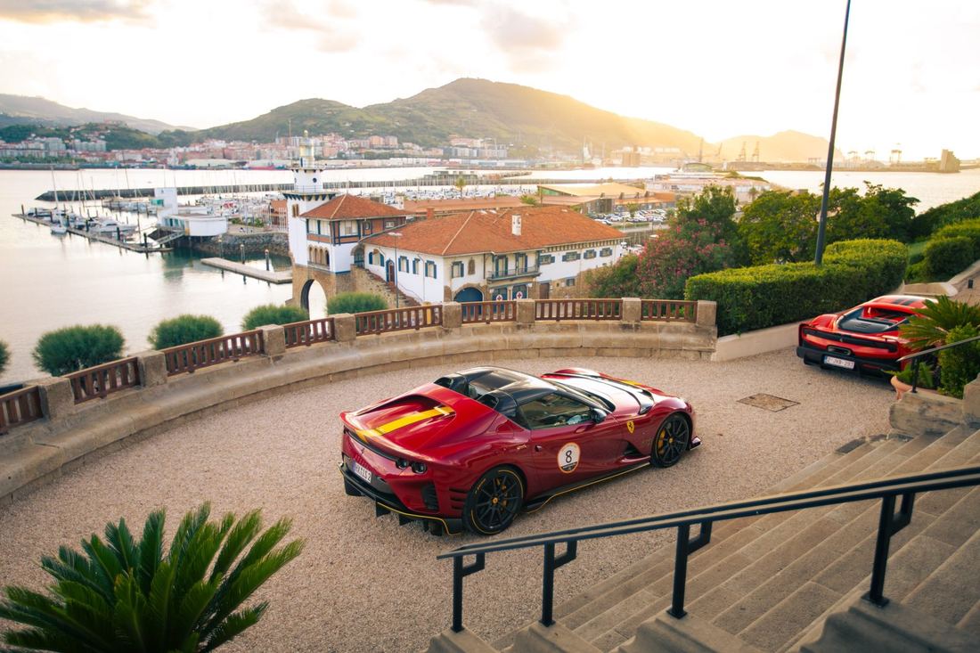 Rode Ferrari 812 met rallynummer op een terras boven een jachthaven bij zonsondergang