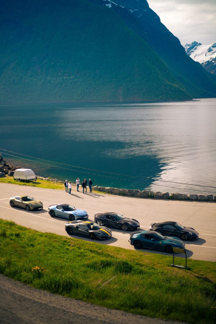 Zes supercars geparkeerd langs een fjord met bergen op de achtergrond