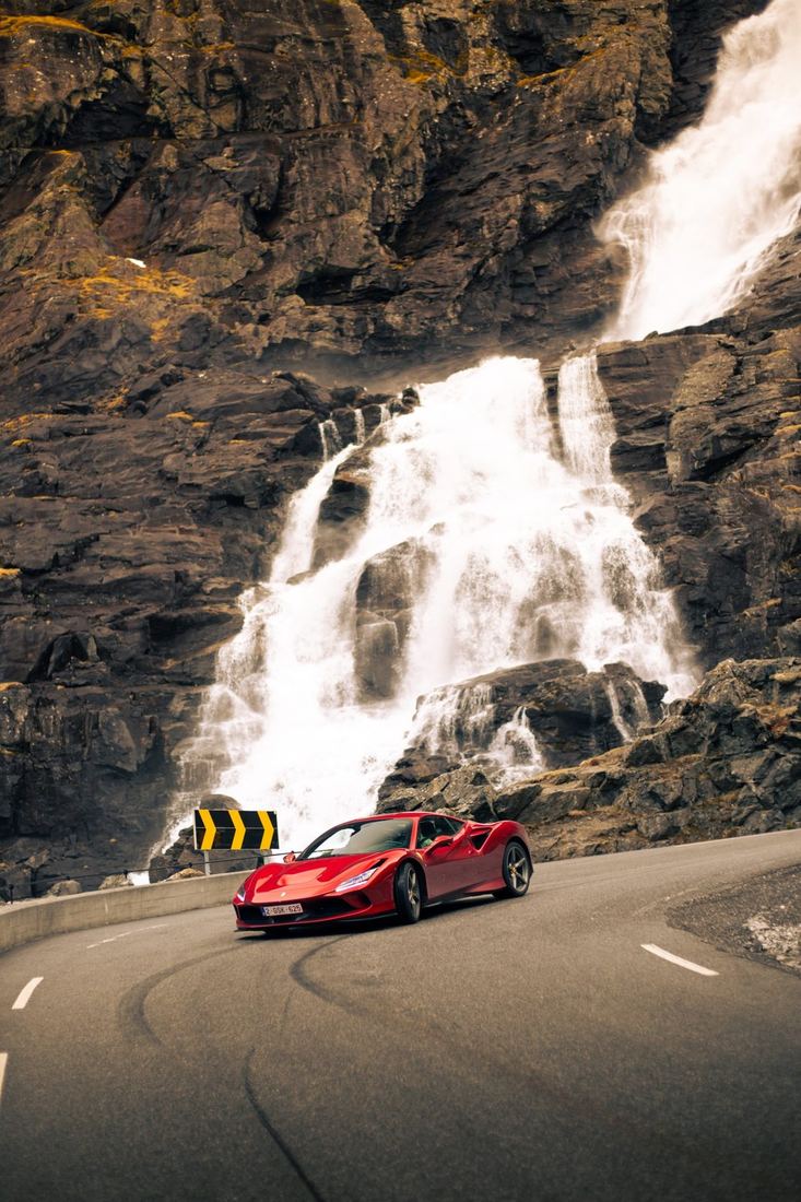 Rode Ferrari F8 Tributo in een bocht voor een waterval