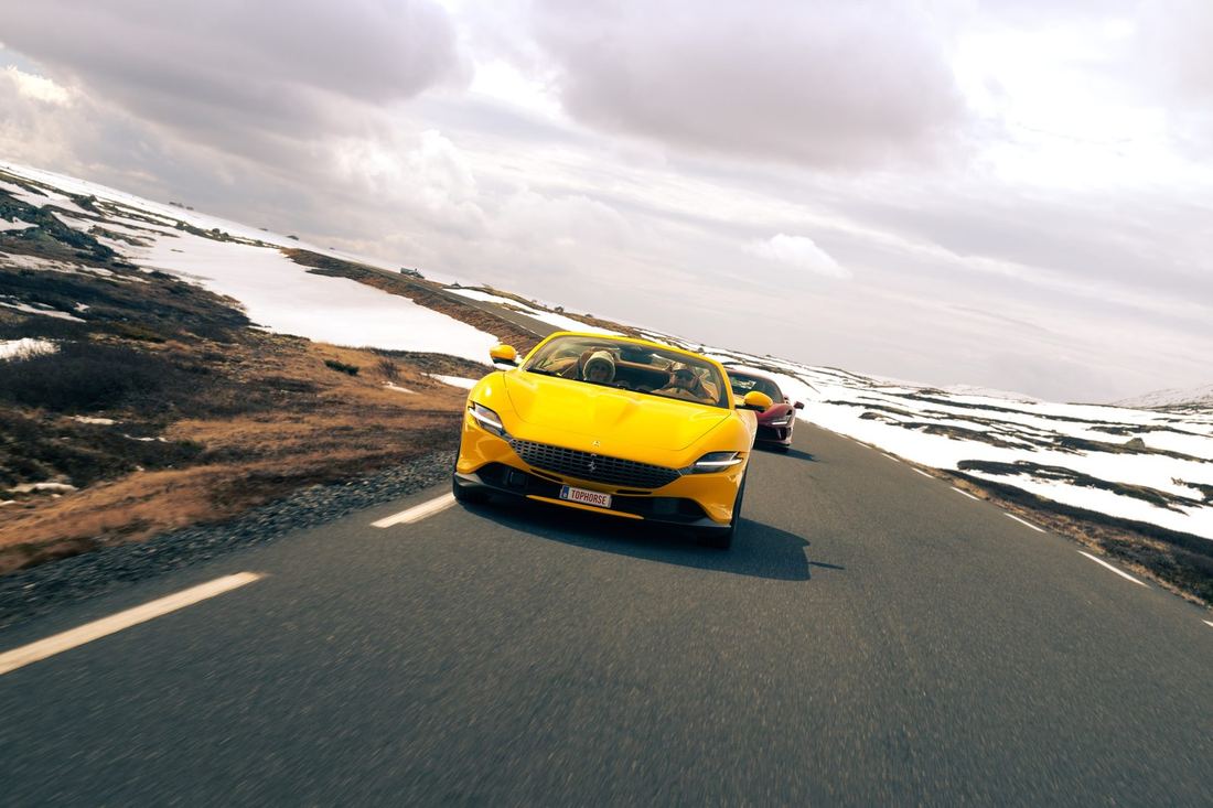 Gele Ferrari Roma Spider met een rode Ferrari erachter op een bergweg