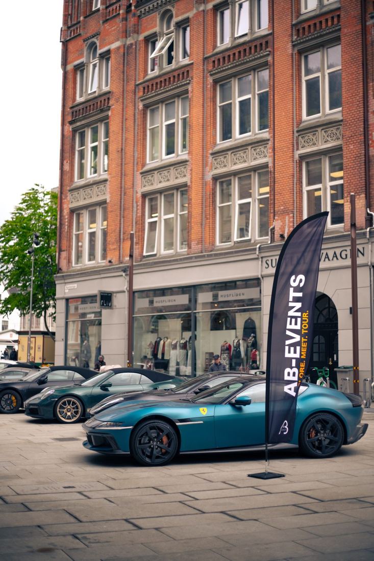 Groene Ferrari en andere supercars bij een AB Events-vlag in de stad