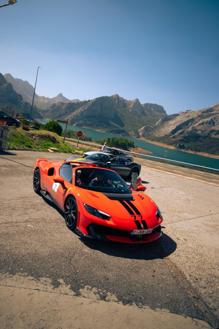 Oranje Ferrari met rallynummer 7 bij een stuwmeer in de bergen