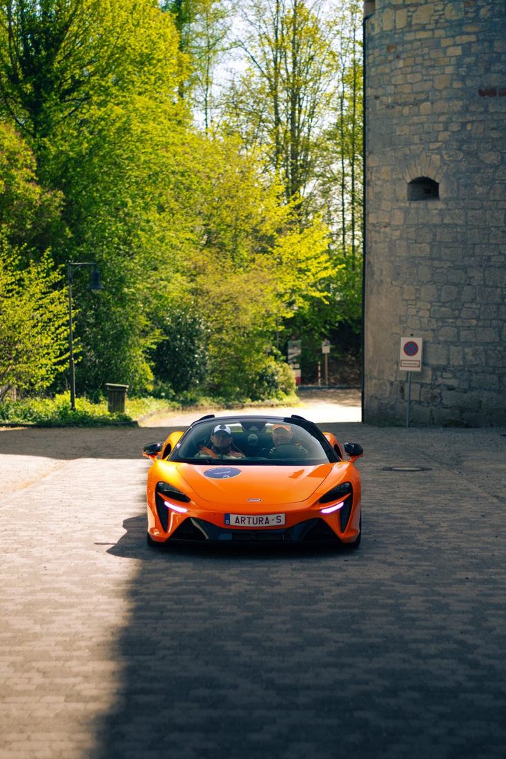 Oranje McLaren Artura rijdt langs de kasteeltoren