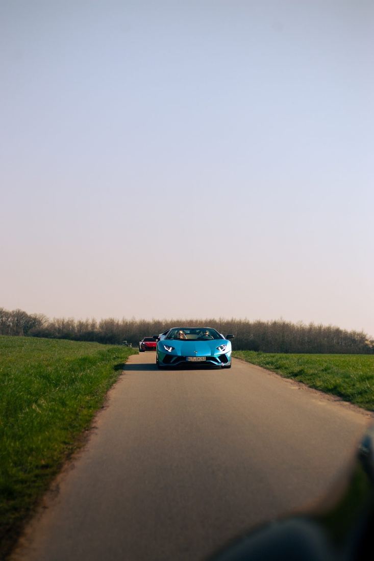 Blauwe Lamborghini Aventador Roadster op een smalle landweg