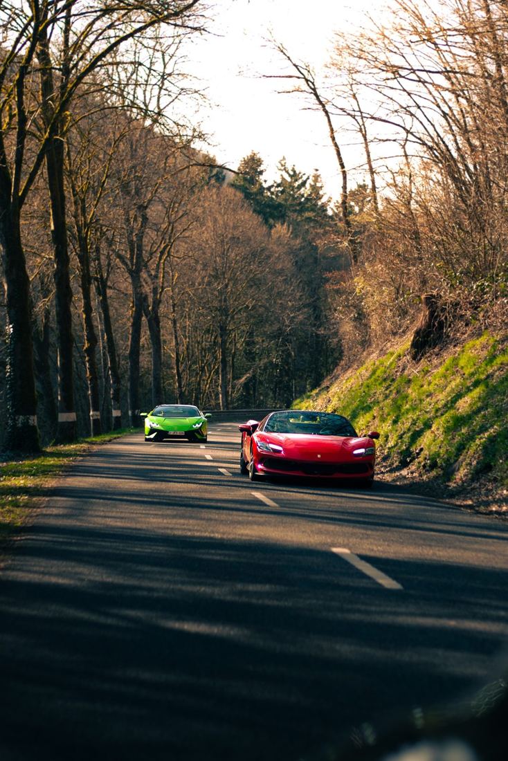 Rode Ferrari 296 en groene Lamborghini op een bosweg