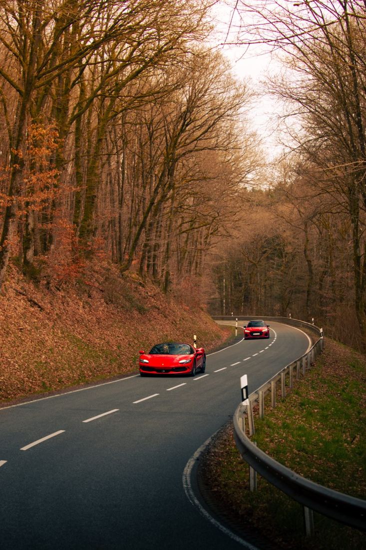 Rode Ferrari 296 en Audi RS6 op een bochtige bosweg