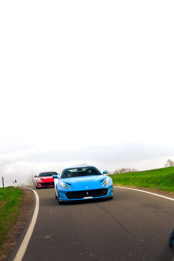 Blauwe en rode Ferrari 812 op een glooiende landweg