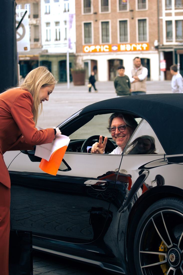 Lachende deelnemer in zijn Porsche bij de ontvangst