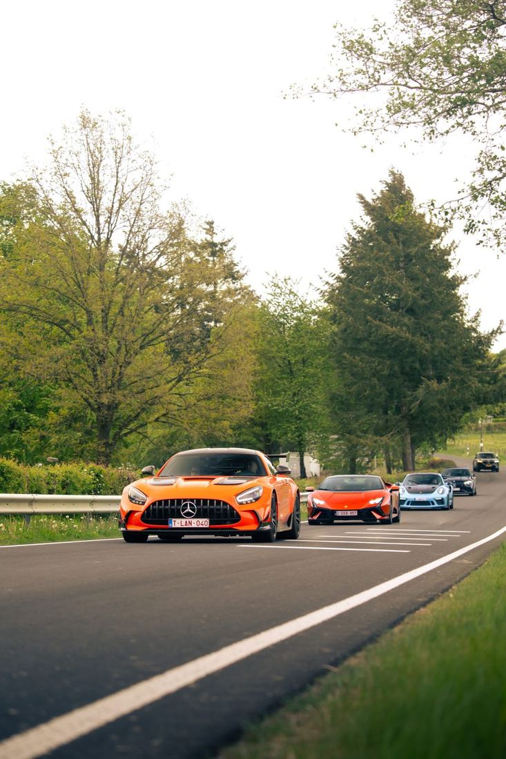 Oranje Mercedes-AMG met een Lamborghini en Porsche erachter op de weg