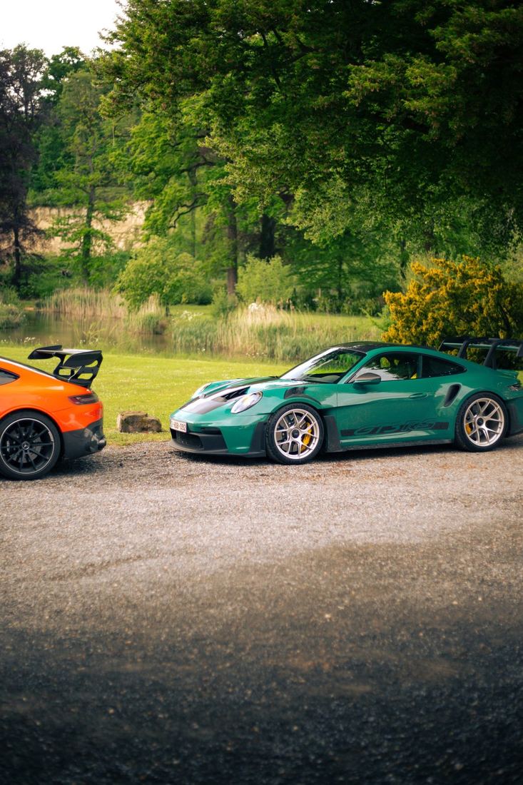 Oranje Mercedes-AMG en groene Porsche GT3 RS in het park