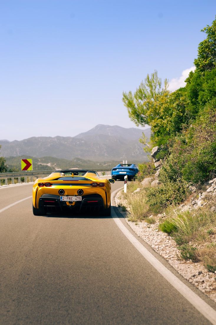 Gele SF90 Spider en blauwe 812 GTS op een kustweg in de bergen